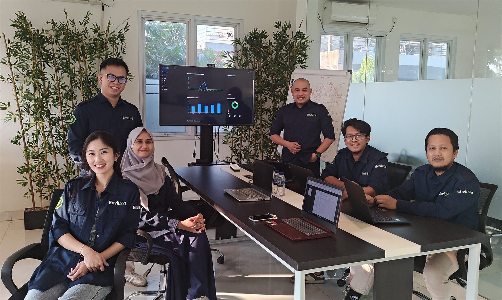 EnviLog team in branded shirts gathered around the logistics platform dashboard